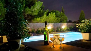A poolside setting with a bottle and two glasses, surrounded by potted plants and a wooden fence. - Four seasons House (Corfu)