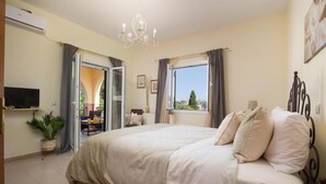 A bedroom with a large bed, a TV, a chandelier, and a view of the outdoors. - Four seasons House (Corfu)