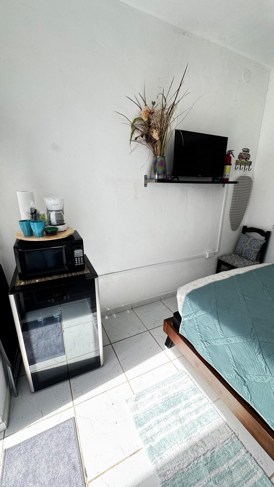 A bedroom with a bed, a TV on a shelf, a coffee maker, and a microwave.