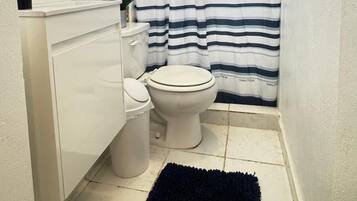 A small bathroom with a white toilet, a white sink, a black rug, and a striped shower curtain.