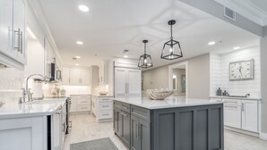 A modern kitchen with white cabinetry, a large island, and pendant lighting. - Inn at Crystal Beach 506 * Gulf Front with Beach Chair Set. Onsite dining! (Destin)