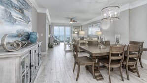 A spacious dining area with a large wooden table and chairs, a chandelier, and a view to the outside. - Inn at Crystal Beach 506 * Gulf Front with Beach Chair Set. Onsite dining! (Destin)