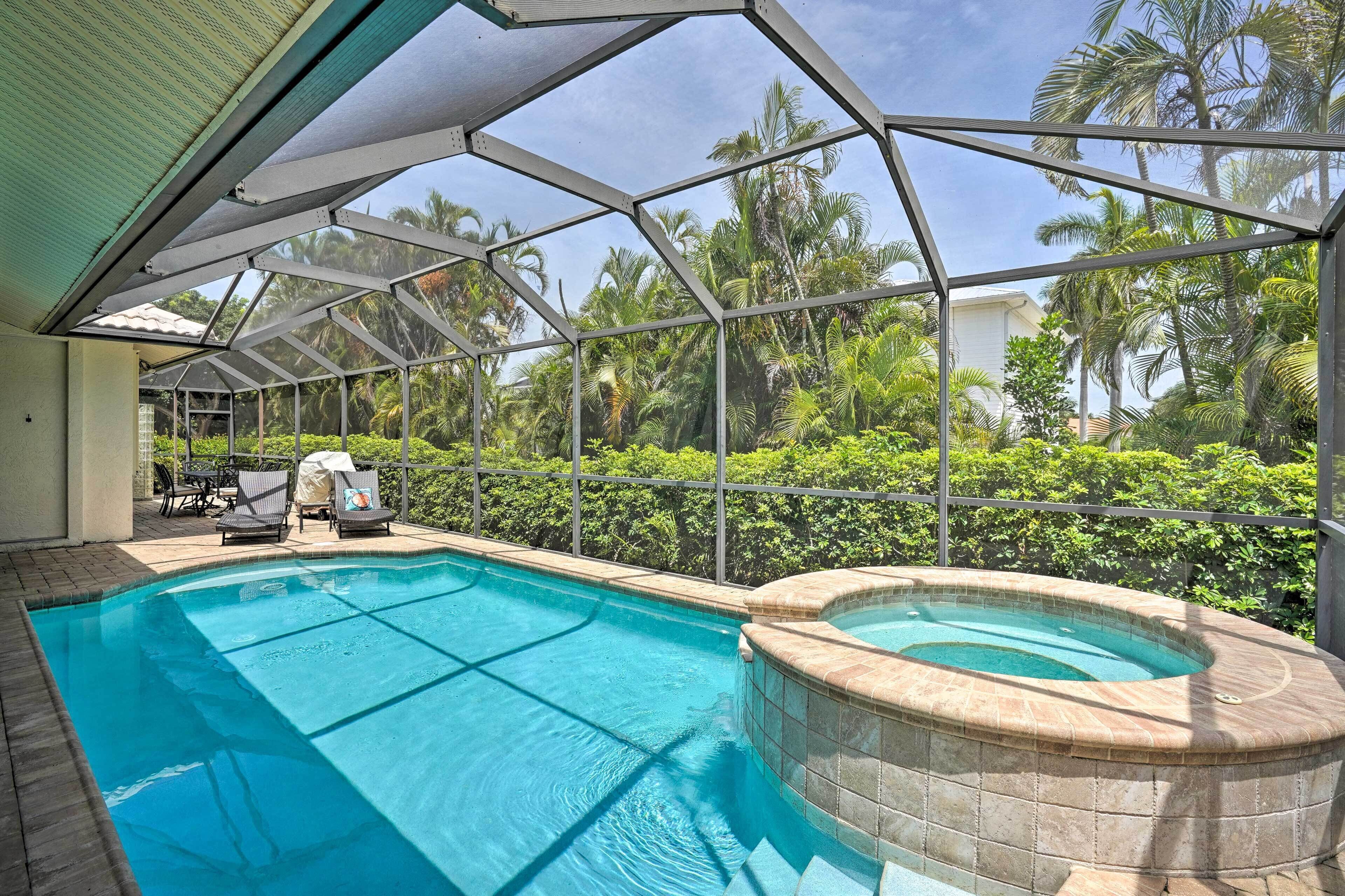 Piscina com banheira de hidromassagem, cercada por um compartimento de vidro e palmeiras.