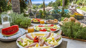 An outdoor dining area with a variety of food items, a pitcher of milk, and a view of a pool and landscape. - Villa Elisa, View+Hidden in Trees! (Perama)