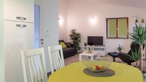 Un salon moderne avec un canapé, un téléviseur et une table à manger agrémentée d’un panier de fruits.