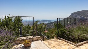 Un escalier en pierre mène à un balcon d’où l’on peut admirer un paysage urbain côtier, avec une montagne qui se profile à l’horizon.