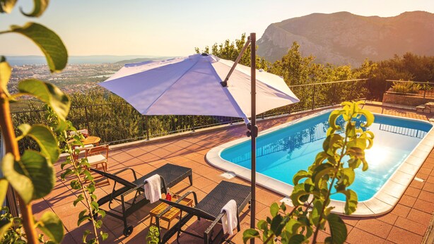 Un espace piscine aménagé avec des chaises longues, une table et un grand parasol.