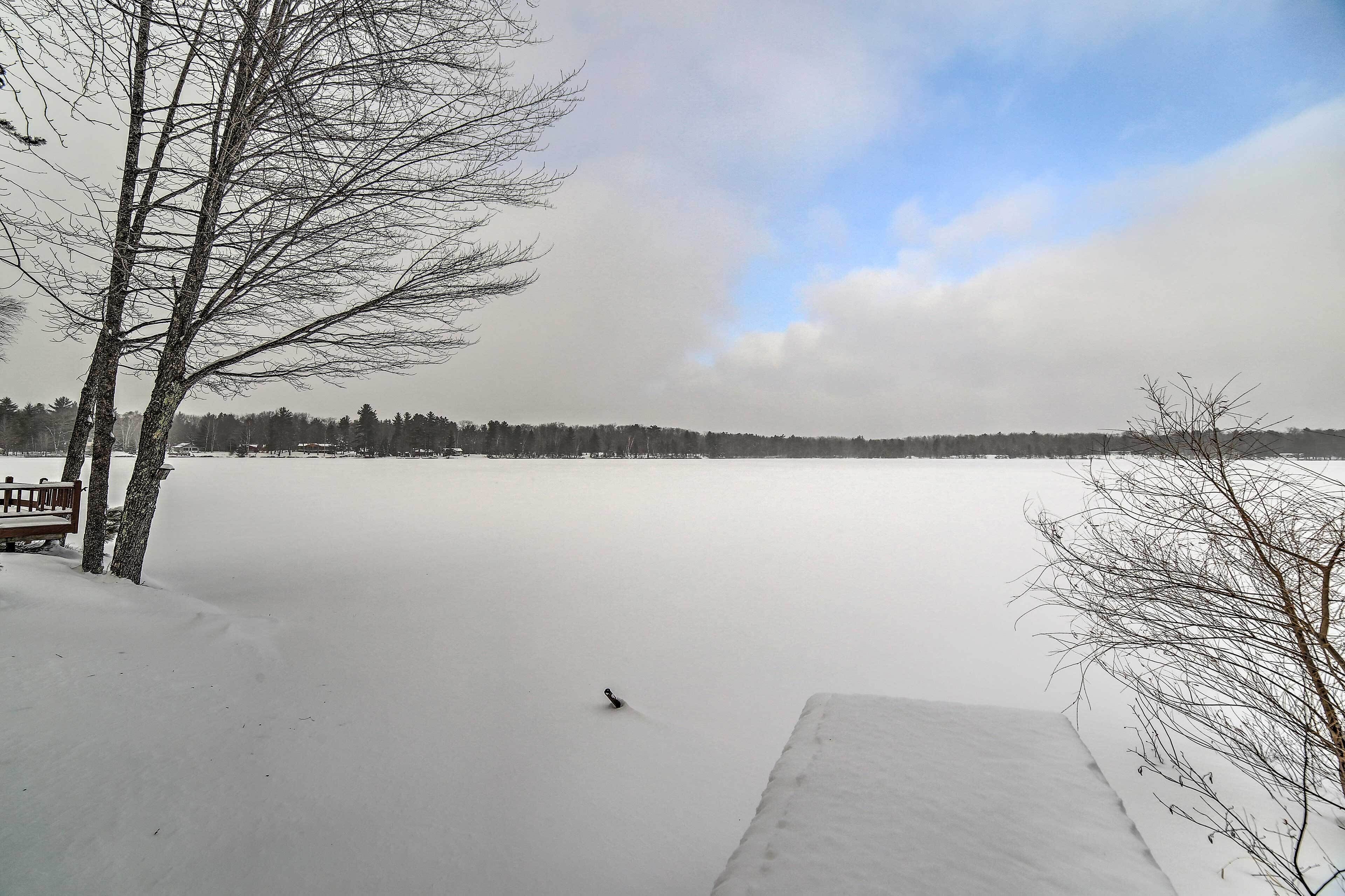 A snow-covered landscape with a bench and a wooden dock extending into a frozen lake.