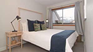 Un dormitorio con cama, mesita de noche, lámpara y ventana con cortinas.