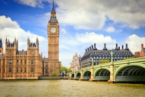 A view of the Houses of Parliament and Big Ben across the River Thames, with a green bridge in the foreground.