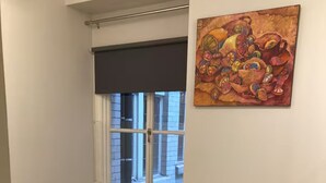 Une petite chambre à coucher, bien rangée, avec un lit simple, une fenêtre donnant sur l’extérieur, un radiateur et un tableau accroché au mur.