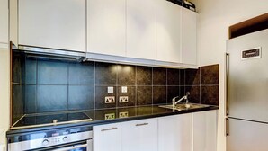 Une cuisine moderne avec des meubles blancs, un plan de travail noir et des appareils en acier inoxydable, notamment une cuisinière, un four et un réfrigérateur.