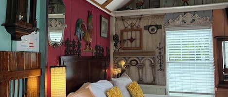 A bedroom with a large bed, wooden beams, a red wall, and various decorative items.