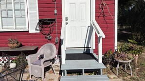 A red house with a white door, a porch with a bench, and outdoor furniture. - The Red Cottage ~ 5 min. stroll to Historic St. George Street - on site parking (Saint Augustine)