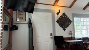 A room with a white door, a mounted television, a decorative wall piece, and a table with a chair. - The Red Cottage ~ 5 min. stroll to Historic St. George Street - on site parking (Saint Augustine)