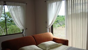 Ein Schlafzimmer mit Bett, Vorhängen und Blick auf Grün.