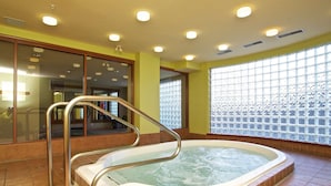 Ein Whirlpool in einem Zimmer mit gelben Wänden, großen Fenstern und einem Metallgeländer.