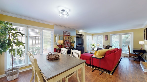 A living room with a wooden dining table, red sofa, and a TV.