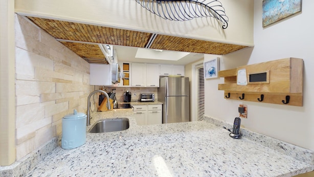 A kitchen with granite countertops, a stainless steel refrigerator, and a hanging rack with hooks. - Nicely Updated First Floor Villa! (Hilton Head)