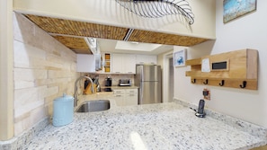 A kitchen with granite countertops, a stainless steel refrigerator, and a hanging rack with hooks.