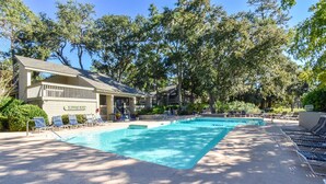 A swimming pool with lounge chairs, a building with a 'No Lifeguard on Duty' sign, and surrounding trees. - Nicely Updated First Floor Villa! (Hilton Head)