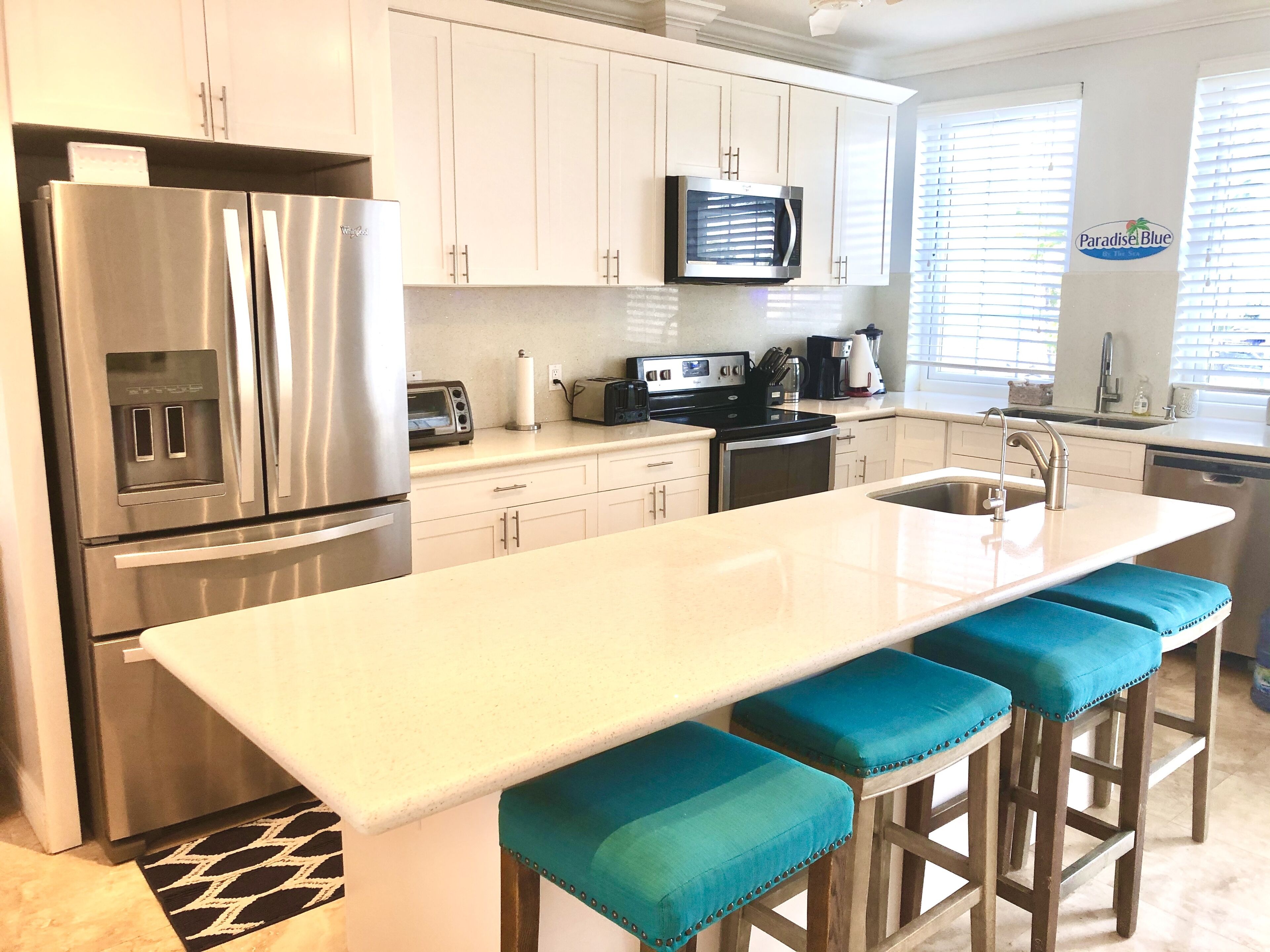 A modern kitchen with stainless steel appliances, a large island with bar stools, and a view of the outdoors through the window.