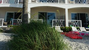 Un hotel frente a la playa, con una palmera, sillas de playa y un cielo azul cristalino.