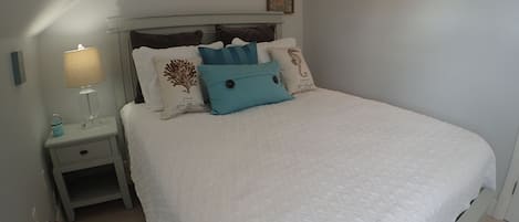 A neatly made bed with a white quilt, a bedside table with a lamp, and a wall-mounted mirror.