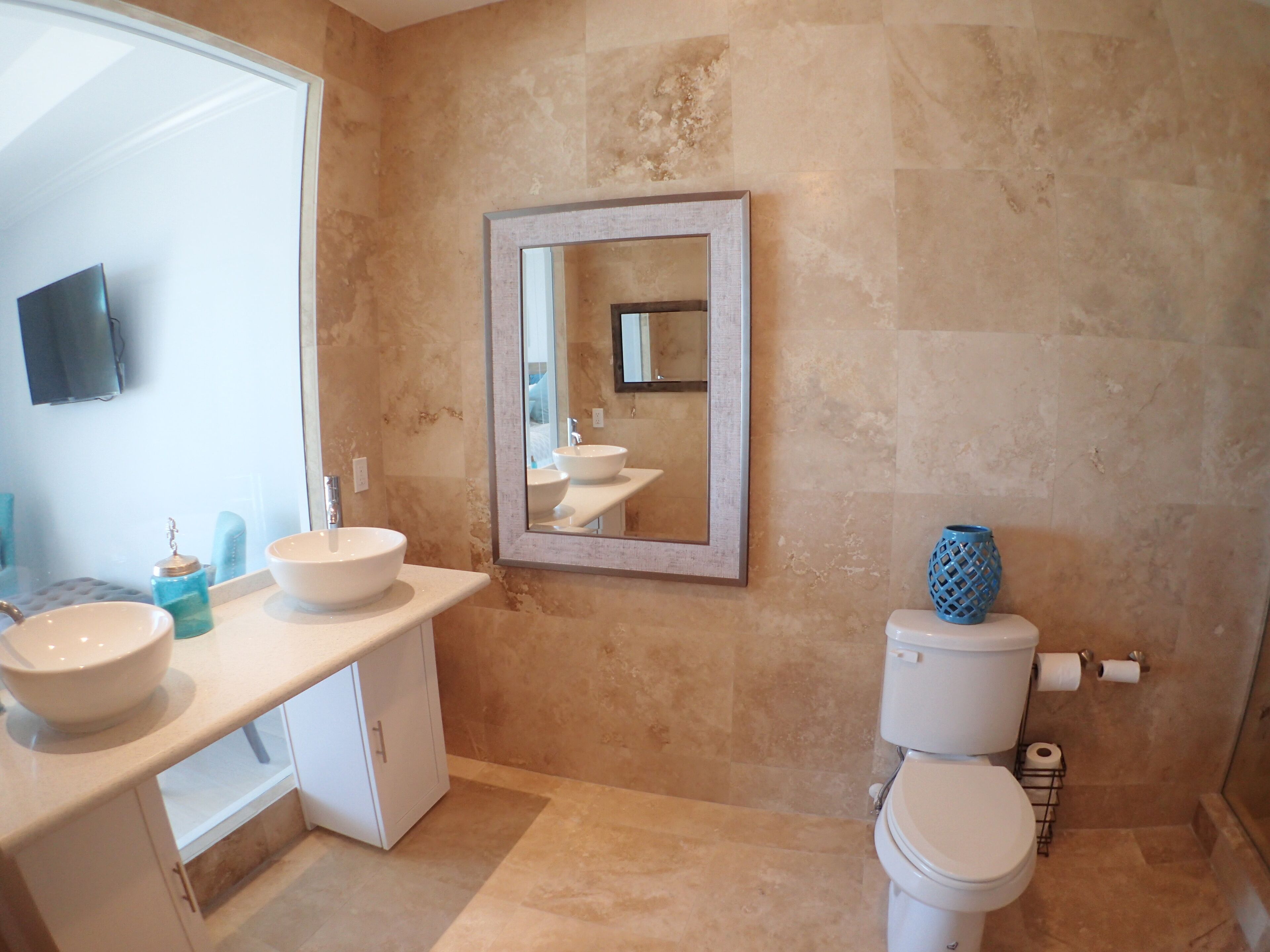 Un baño con un espejo grande, dos lavamanos, un inodoro y un jarrón azul decorativo.