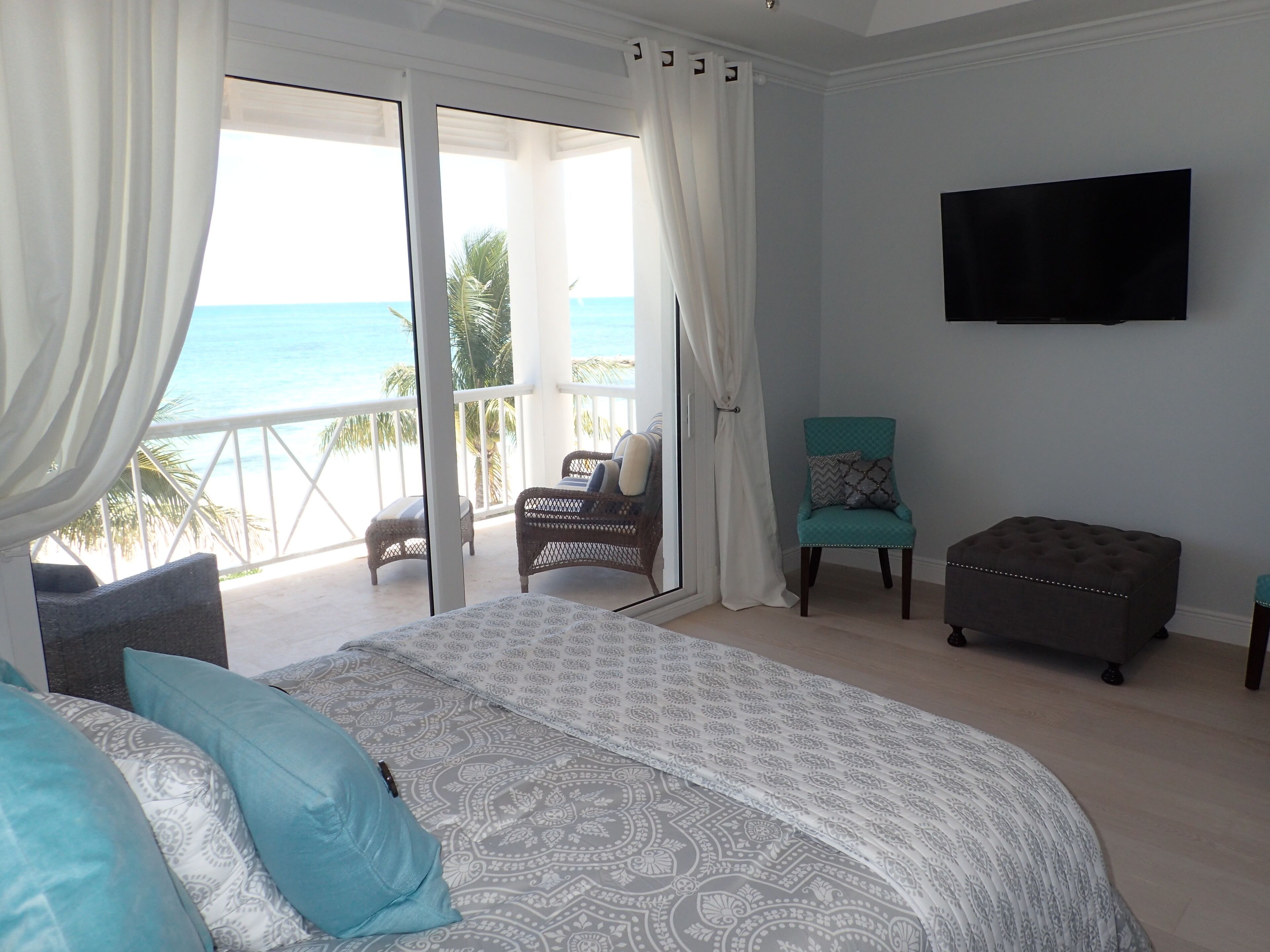 Quarto com cama, cadeira, banco, televisão e varanda com vista para o mar.