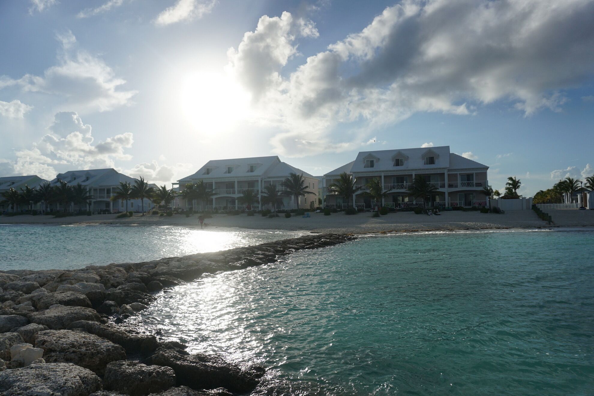 A beachfront property with multiple buildings, a rocky shoreline, and a clear sky.