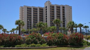 Un hotel de varios pisos con una fachada uniforme, rodeado de jardines ajardinados y palmeras.