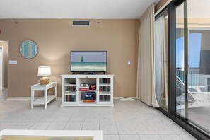 A living room with a television, bookshelves, a clock, and a view of the outdoors.