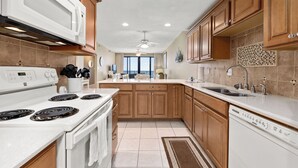 Una cocina moderna con estufa, microondas y lavavajillas, armarios de madera y un amplio ventanal con vistas.