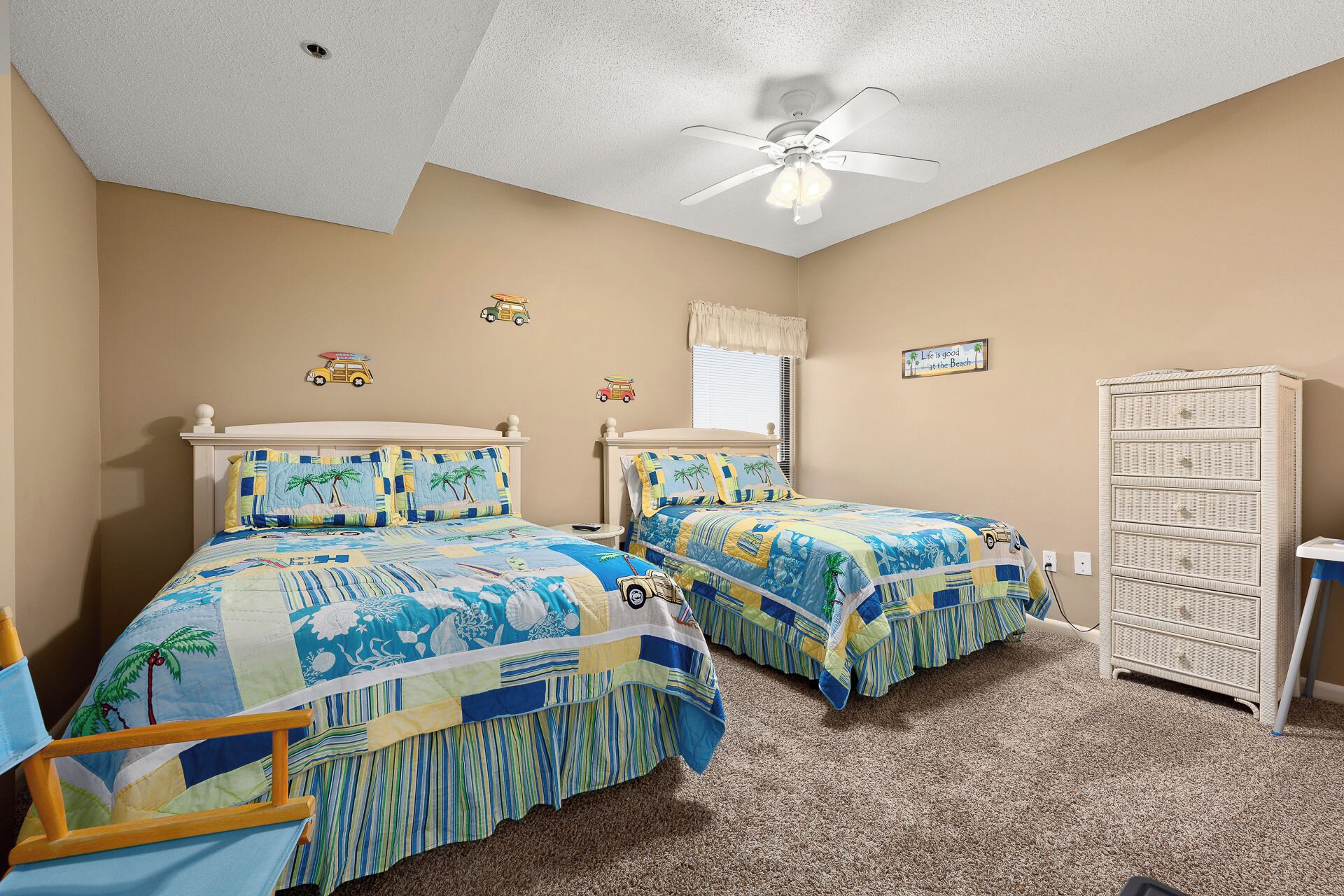 A bedroom with two beds, a ceiling fan, a window with blinds, and a wicker dresser.
