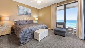 Un dormitorio con cama, mesita de noche, una silla, una maleta y vista al océano.