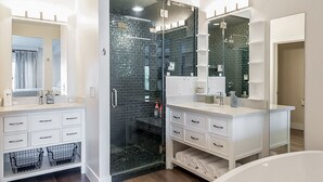 Un baño moderno con ducha de vidrio, muebles blancos y un espejo grande.