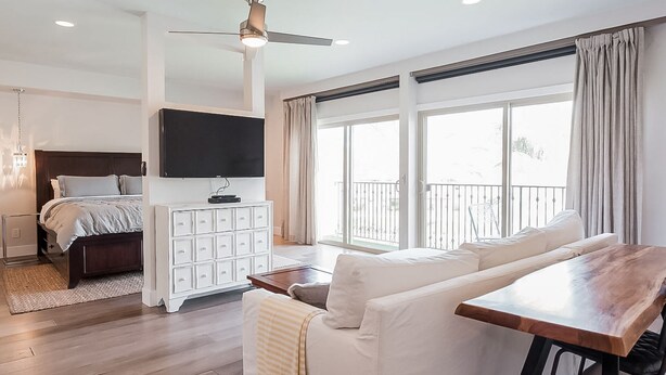 Un dormitorio moderno con cama, televisor, cómoda y balcón con cortinas.