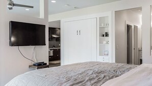 Un dormitorio moderno con una cama grande, un televisor en la pared, un armario y una estantería empotrada.