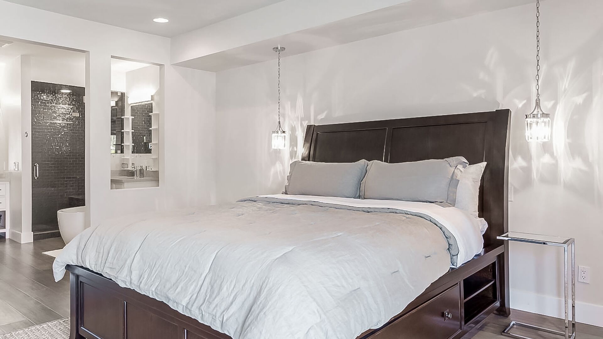 A modern bedroom with a large bed, a dark headboard, and pendant lights.