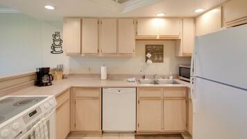 A kitchen with light wooden cabinets, a white dishwasher, a stove, a sink, and a refrigerator.