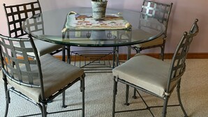Een eetruimte met een glazen tafel, vier metalen stoelen, een geweven pot met een plant en een lijst met een landschapsafbeelding aan de muur.