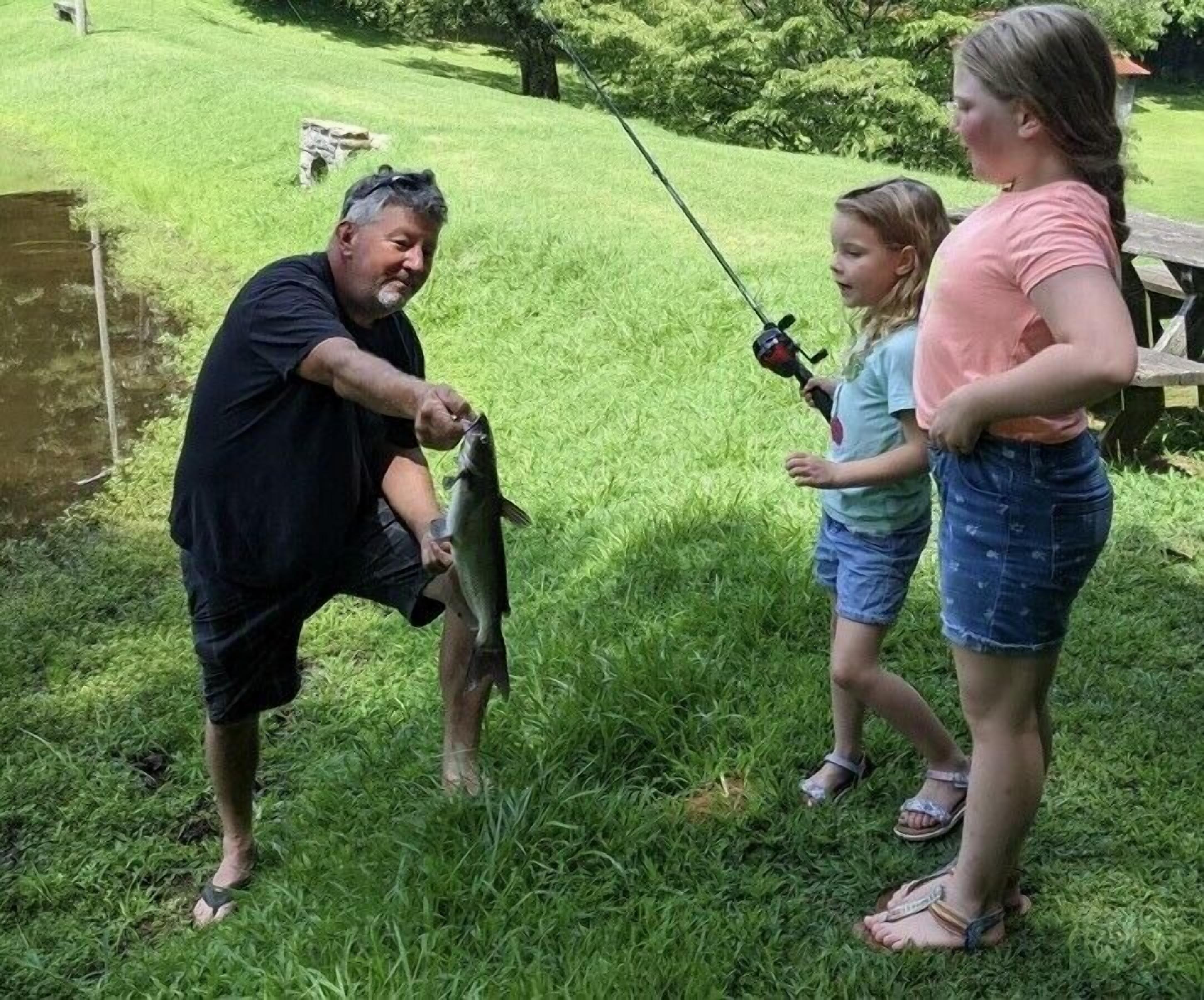 A man holding a fish, a child with a fishing rod, and a woman standing by.