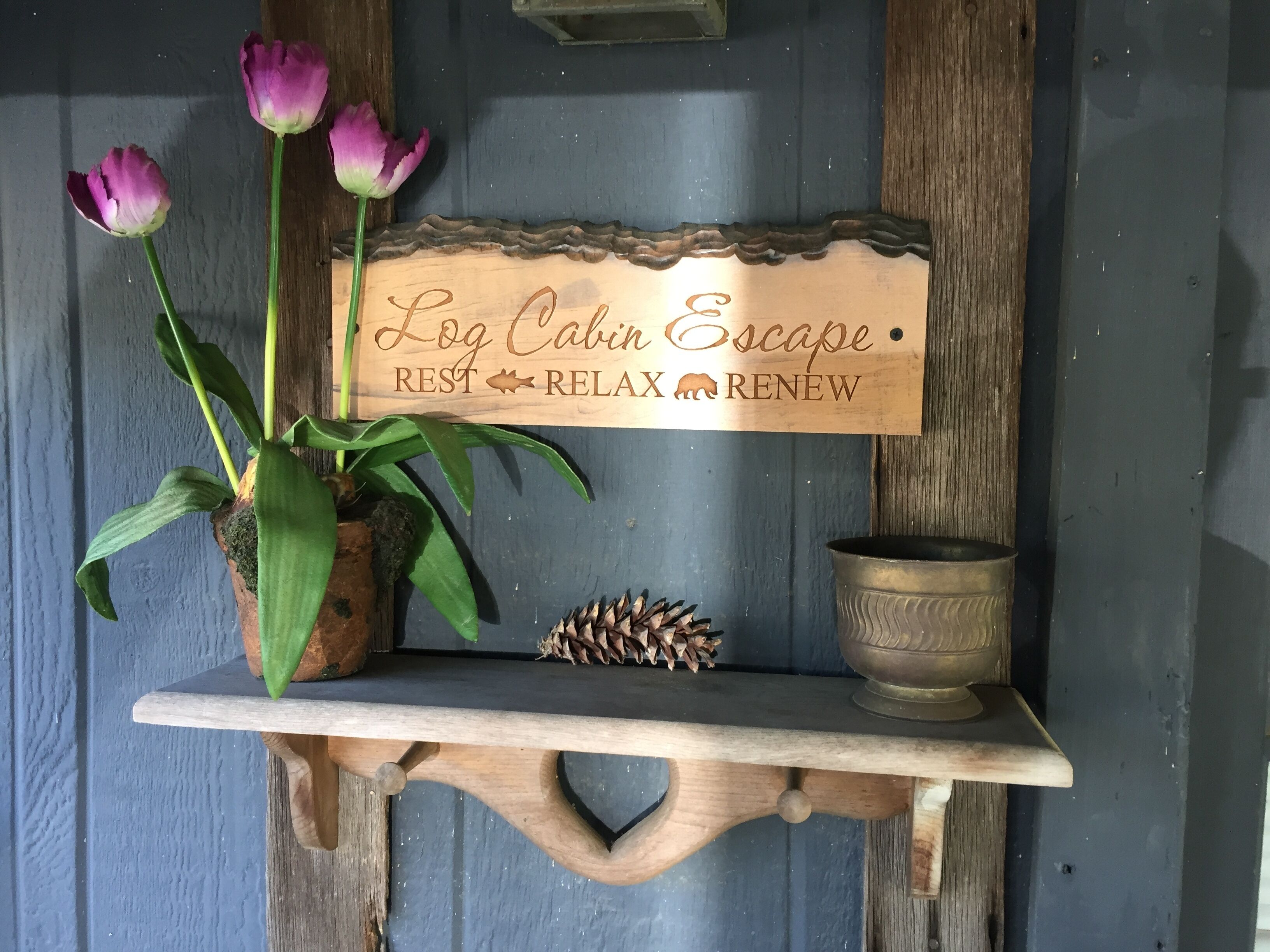 A wooden sign with the text "Log Cabin Escape REST RELAX RENEW" on a shelf.