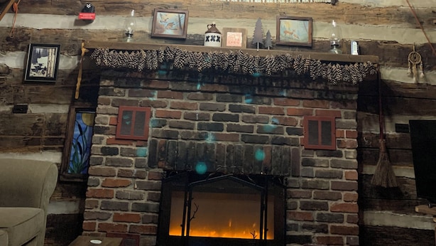 L’intérieur d’un chalet rustique en rondins de bois, avec une cheminée, des murs en bois et un luminaire suspendu.