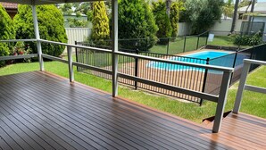 A wooden deck with a metal railing, a pool, and a grassy yard with trees.