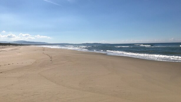 A wide, sandy beach with gentle waves and a clear sky.