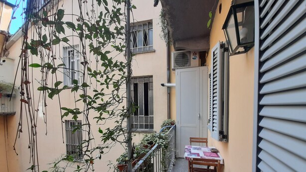 Een smal balkon met een tafel en stoelen, omgeven door potplanten en klimop.