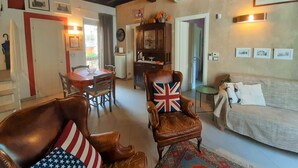 Een gezellige woonkamer met een houten plafond, een eethoek met een tafel en stoelen, een bank en een decoratieve fauteuil met een Union Jack kussen.