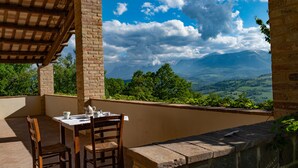 A terrace with a table set for two, overlooking a mountainous landscape.